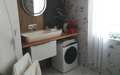 Wnętrze łazienki z nowoczesną umywalką, pralką i drewnianymi akcentami.