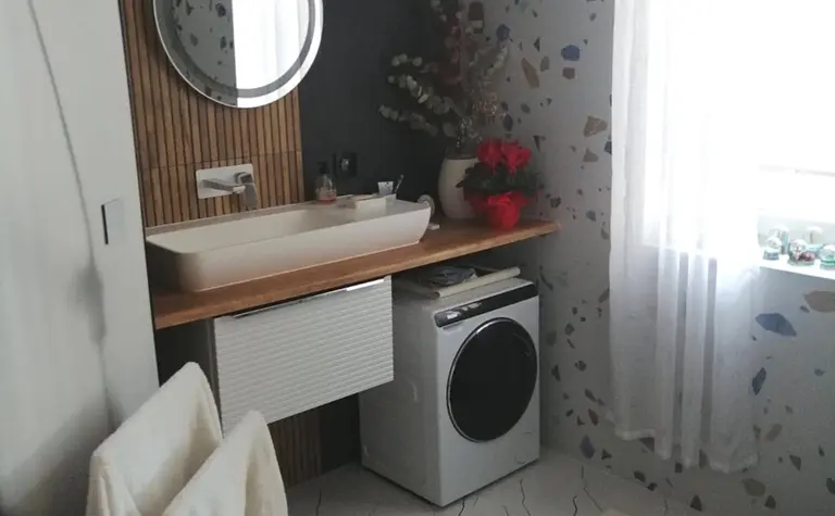 Wnętrze łazienki z nowoczesną umywalką, pralką i drewnianymi akcentami.