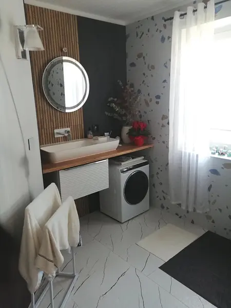 Wnętrze łazienki z nowoczesną umywalką, pralką i drewnianymi akcentami.