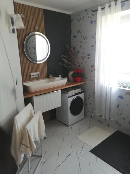 Wnętrze łazienki z nowoczesną umywalką, pralką i drewnianymi akcentami.
