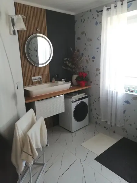 Wnętrze łazienki z nowoczesną umywalką, pralką i drewnianymi akcentami.