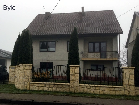 Widok domu z balkonem, ogrodzeniem i zielonymi drzewami, minimalistyczny, nowoczesny.