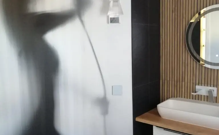 Wnętrze łazienki z drewnianymi akcentami, nowoczesne oświetlenie i okrągłe lustro.