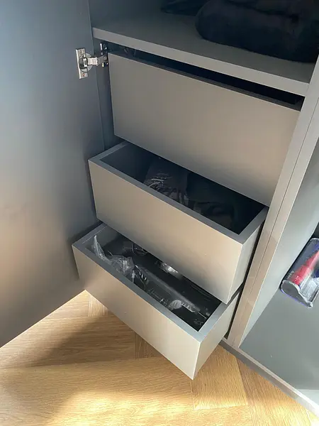 Garderoba w stylu minimalistycznym i nowoczesnym z szarymi szafkami i drewnianą podłogą.