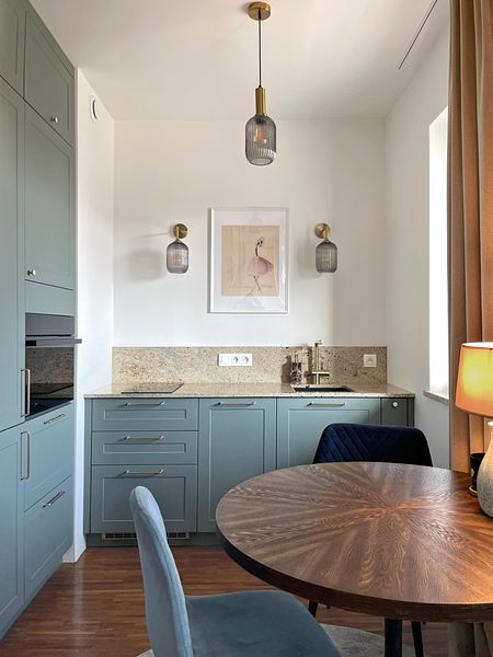 Wnętrze kuchni z niebieskimi meblami, drewnianym stołem i nowoczesnymi lampami.