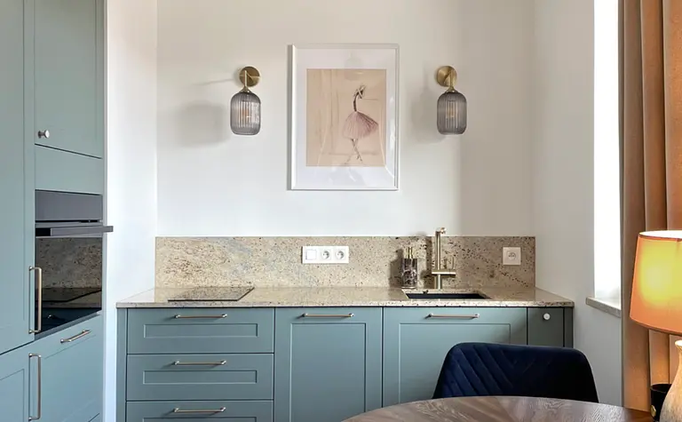 Wnętrze kuchni z niebieskimi meblami, drewnianym stołem i nowoczesnymi lampami.