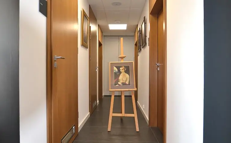 Korytarz w stylu minimalistycznym z obrazem na sztaludze i drewnianymi akcentami.