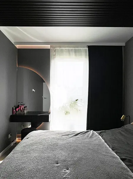 Wnętrze sypialni w stylu minimalistycznym z szarymi ścianami, czarnymi zasłonami i nowoczesnym lustrem.