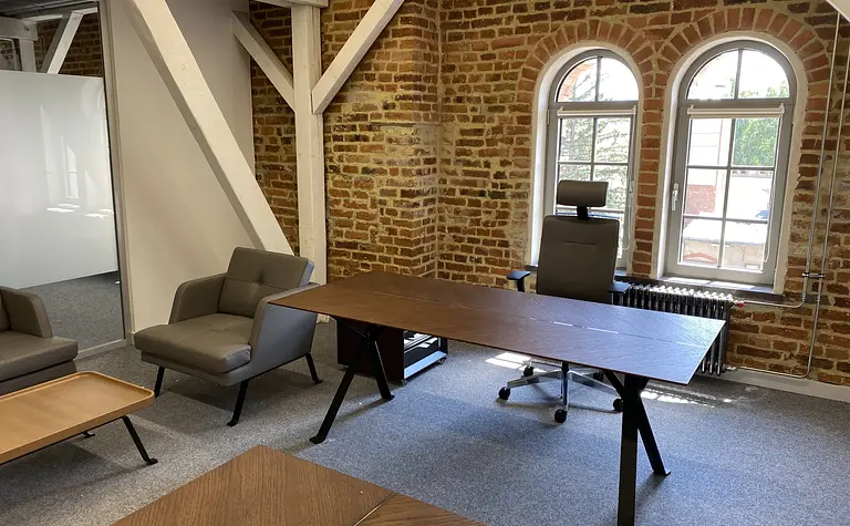 Wnętrze biura w stylu industrialnym z drewnianym biurkiem i szarymi fotelami.