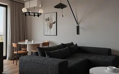 Wnętrze salonu z minimalistycznym wystrojem, industrialnymi akcentami, szarymi ścianami oraz czarną sofą.