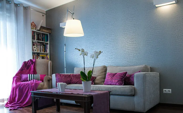 Wnętrze salonu z szarymi ścianami, fioletowymi poduszkami i białymi orchideami.