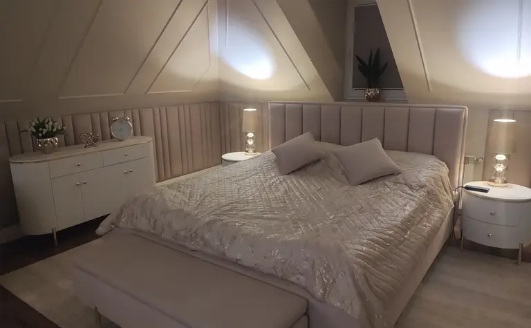 Sypialnia z jasnym łóżkiem, szafką i dekoracjami glamour.