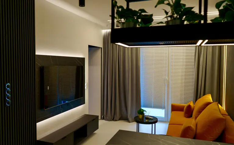 Wnętrze nowoczesnego salonu z szarymi zasłonami, żółtą sofą i stylowym telewizorem.