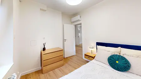 Sypialnia w stylu skandynawskim z beżowymi meblami i niebieską poduszką.