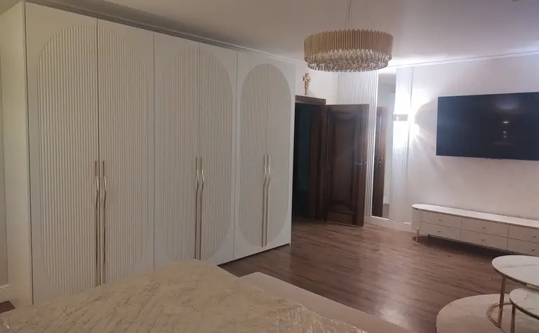Sypialnia w stylu glamour z białymi meblami i drewnianą podłogą.