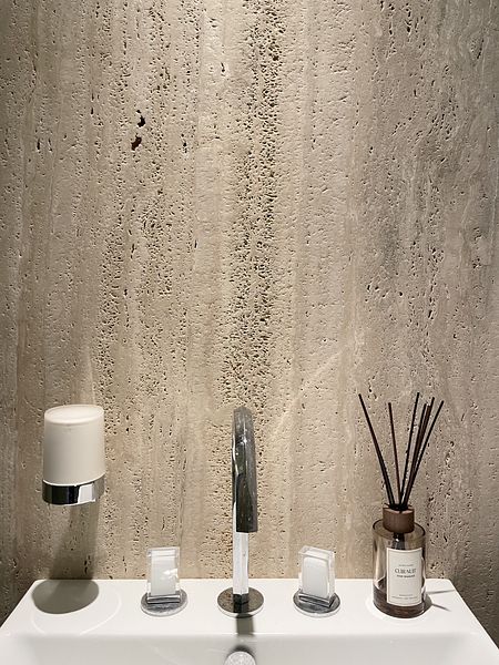 Jasna łazienka z trawertynem na ścianie, chromowaną baterią i dozownikiem by wedodesign.pl