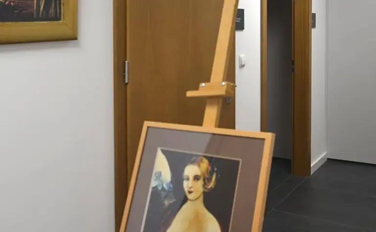 Korytarz w stylu minimalistycznym z obrazem na sztaludze i drewnianymi akcentami.