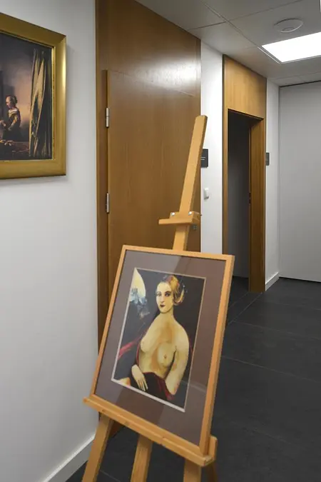 Korytarz w stylu minimalistycznym z obrazem na sztaludze i drewnianymi akcentami.