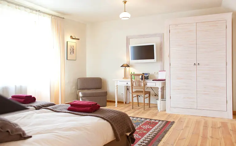 Wnętrze pokoju z elementami boho i minimalistycznymi, z biurkiem i dużym łóżkiem.