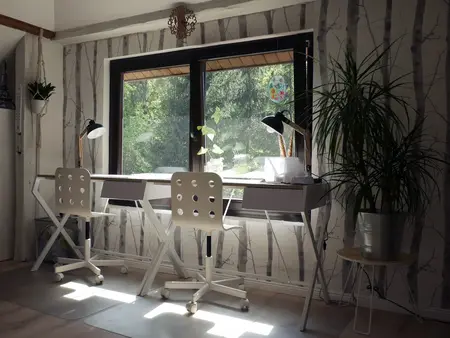 Wnętrze biura ze skandynawskim designem, białe biurka, rośliny i duże okno.