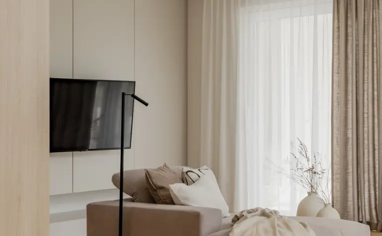 Wnętrze salonu w stylu japandi i minimalistycznym z beżową sofą, drewnianą podłogą i jasnymi zasłonami.