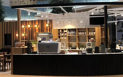 Wnętrze kawiarni z drewnianym barem, minimalistycznym designem i roślinami.