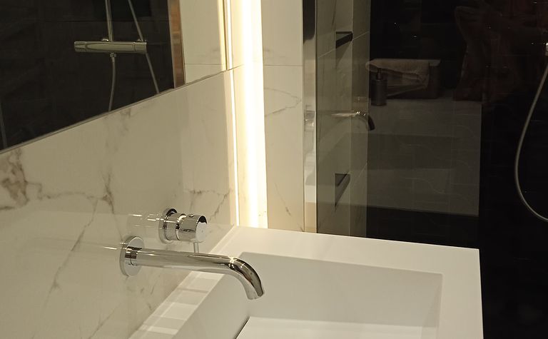 Minimalistyczna łazienka z białą umywalką i nowoczesnym oświetleniem.