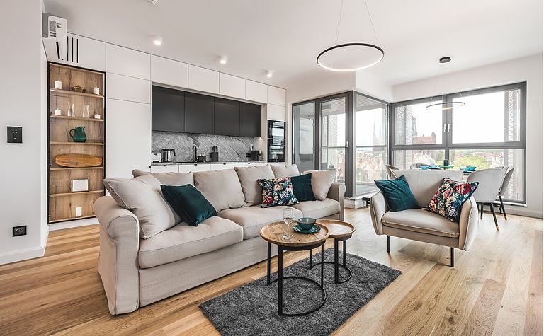 Wnętrze salonu z jasnym sofą, zielonymi poduszkami i drewnianymi akcentami.