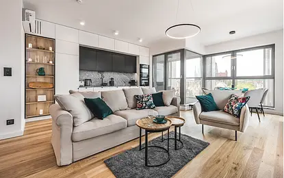 Wnętrze salonu z jasnym sofą, zielonymi poduszkami i drewnianymi akcentami.