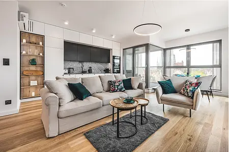 Wnętrze salonu z jasnym sofą, zielonymi poduszkami i drewnianymi akcentami.