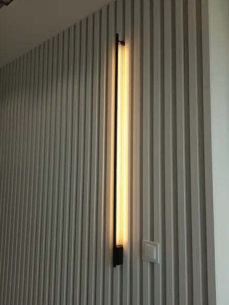 Minimalistyczna ściana z lampą i pionowymi panelami.