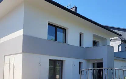Nowoczesny dom z szarymi elementami i dużymi oknami, minimalistyczny styl.