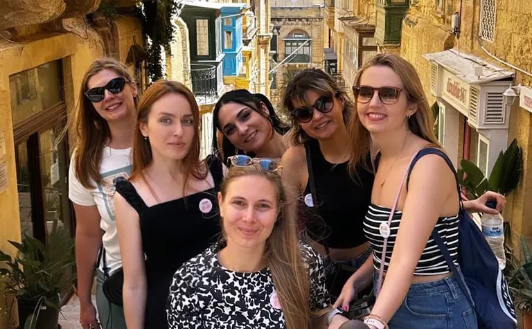 Grupa kobiet na ulicy z kolorowymi budynkami w stylu rustykalnym i eklektycznym.
