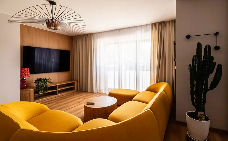 Wnętrze salonu w stylu boho z żółtą sofą i drewnianym stolikiem.