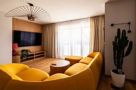 Wnętrze salonu w stylu boho z żółtą sofą i drewnianym stolikiem.