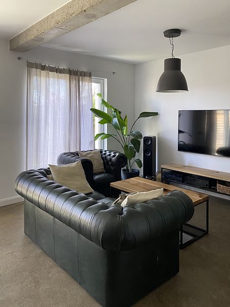 Wnętrze salonu w stylu minimalistycznym z ciemną sofą, drewnianym stołem i roślinami.