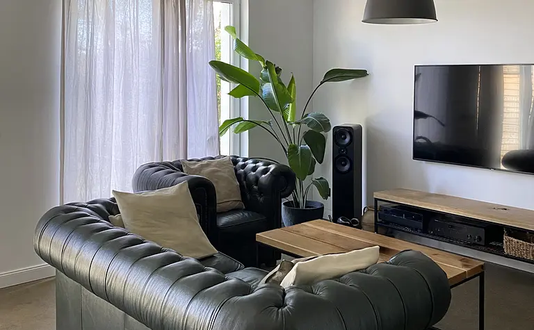 Wnętrze salonu w stylu minimalistycznym z ciemną sofą, drewnianym stołem i roślinami.