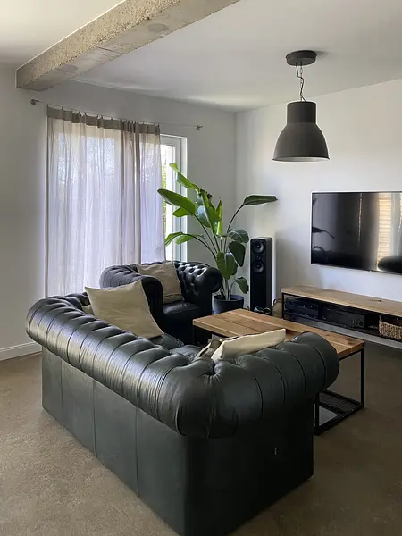 Wnętrze salonu w stylu minimalistycznym z ciemną sofą, drewnianym stołem i roślinami.