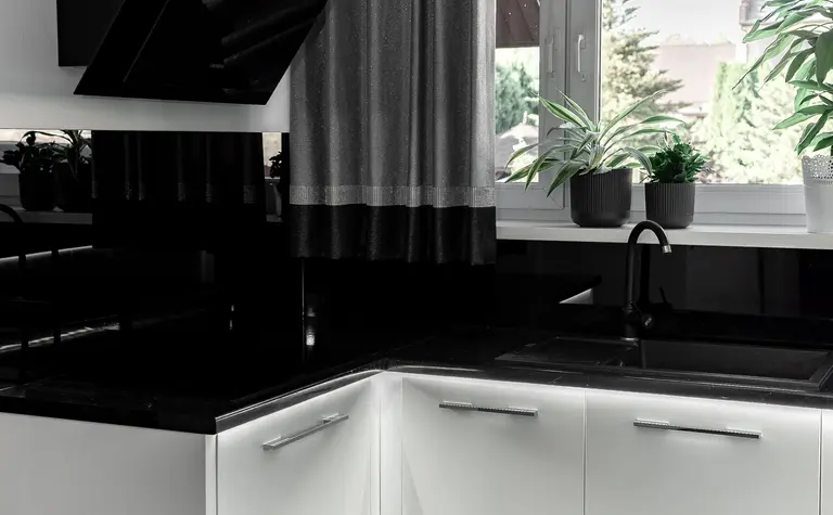 Kuchnia w stylu minimalistycznym z białymi meblami i czarnym blatem.