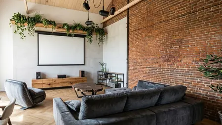 Salon w stylu industrialnym i współczesnym z szarą sofą, ceglaną ścianą i ekranem projekcyjnym