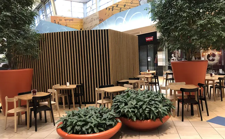 Wnętrze kawiarni z drewnianymi stołami i dużymi roślinami. Styl japandi, minimalistyczny, nowoczesny.