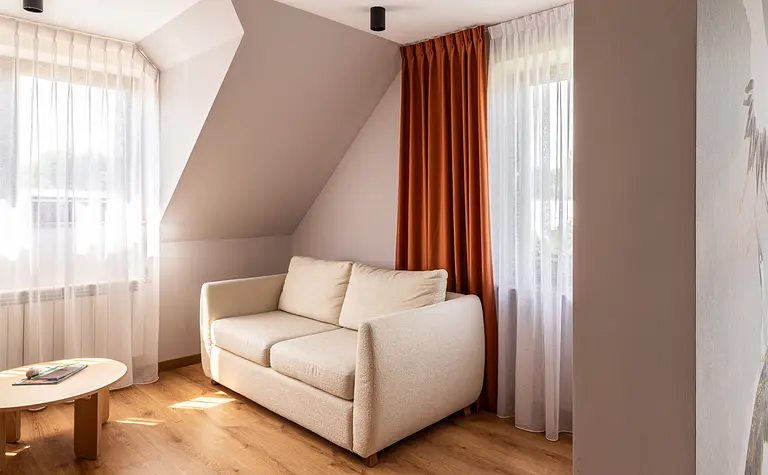 Wnętrze poddasza z beżową sofą, pomarańczowymi zasłonami w stylu boho i skandynawskim.