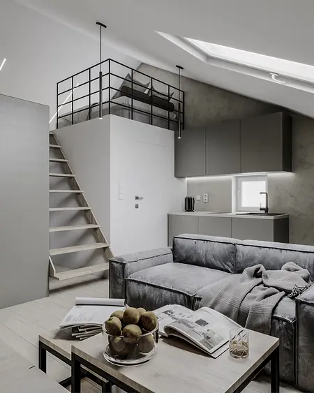 Wnętrze z aneksem kuchennym, szarym sofa i loftowym łóżkiem