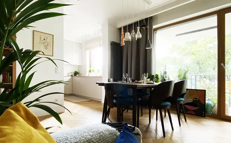 Wnętrze jadalni z minimalistycznym designem, drewnianym stołem, kolorowymi poduszkami.