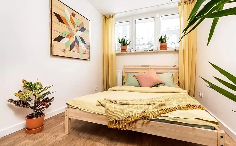 Sypialnia z eklektycznym wystrojem, łóżkiem, roślinami i kolorowymi detalami.