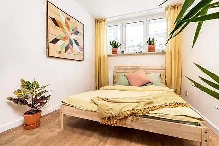 Sypialnia z eklektycznym wystrojem, łóżkiem, roślinami i kolorowymi detalami.