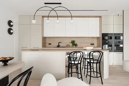 Współczesna kuchnia z białymi meblami, drewnianym blatem i czarnymi akcentami.