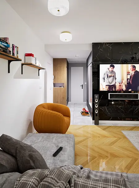 Wnętrze nowoczesnego salonu z brązowym fotelem, telewizorem i drewnianą podłogą.