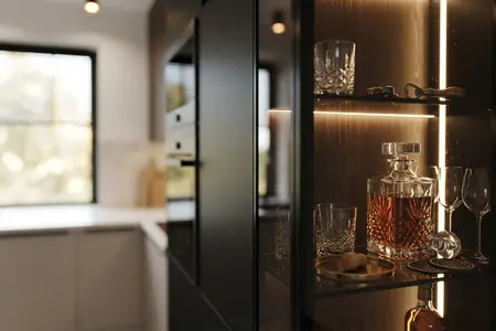 Współczesny i nowoczesny barek z karafką whisky, szklankami i podświetloną półką obok białej kuchni