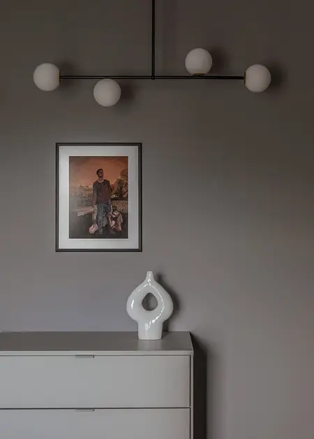 Minimalistyczne wnętrze z szaro-białą komodą, nowoczesnym oświetleniem i obrazem.